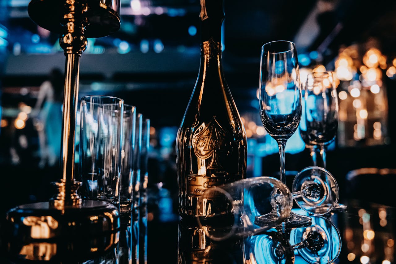 A gold champagne bottle with elegant wine glasses on a reflective surface, exuding luxury.