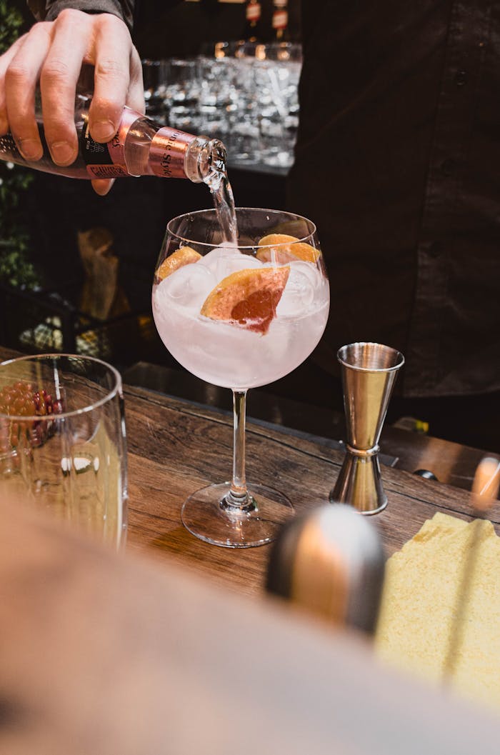 services-04 Close-up of a bartender pouring a grapefruit cocktail in a stylish bar setting.